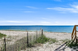 A beach with a wooden fence and a bench, leading to the ocean.