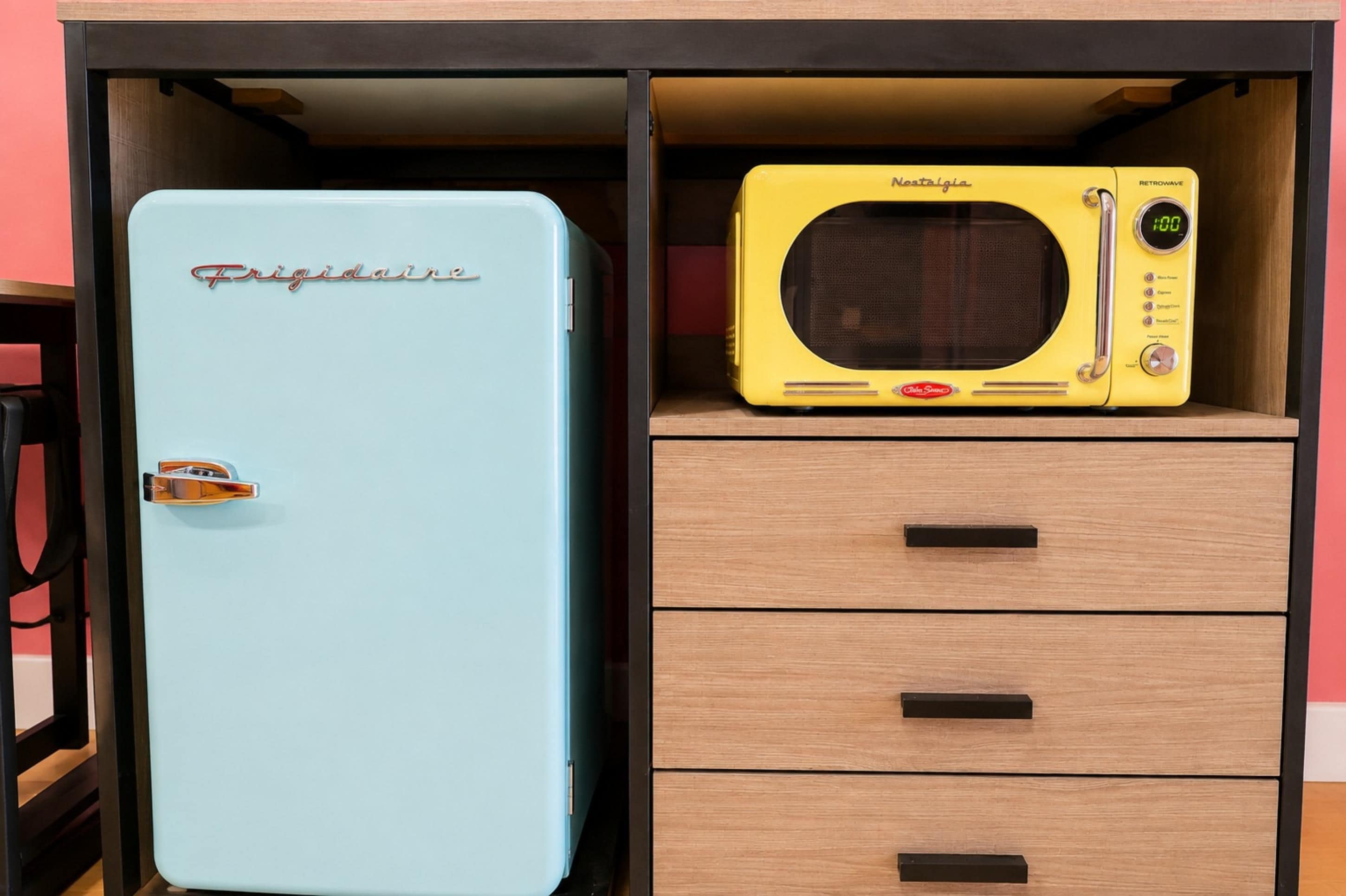 Et blått kjøleskap med merkenavnet 'Frigidaire' og en gul retrowave mikrobølgeovn på toppen av et trehytte med skuffer.