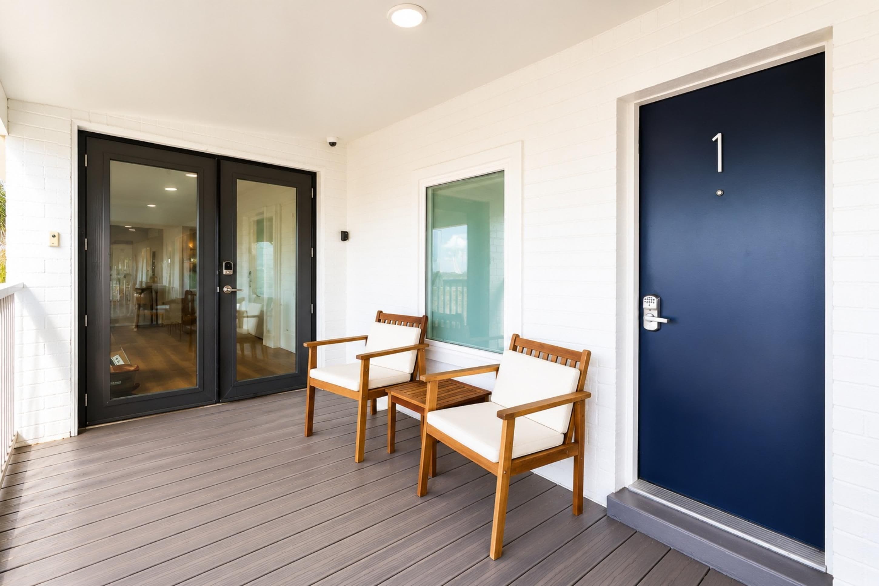 Una terraza de madera con dos sillas y una puerta con cerradura electrónica.