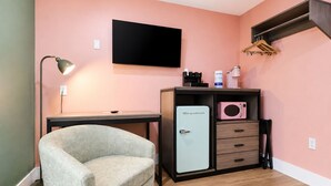 A room with a desk, a chair, a kitchenette with a fridge, a microwave, and a TV mounted on the wall. - The Blu - A Boutique Motel (Port St. Joe)