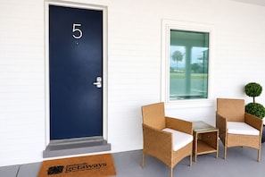 A dark blue door with the number 5, a small table with chairs, and a window with a view of palm trees. - The Blu - A Boutique Motel (Port St. Joe)