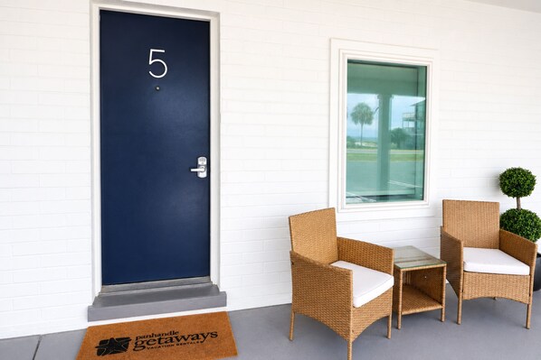 A dark blue door with the number 5, a small table with chairs, and a window with a view of palm trees.