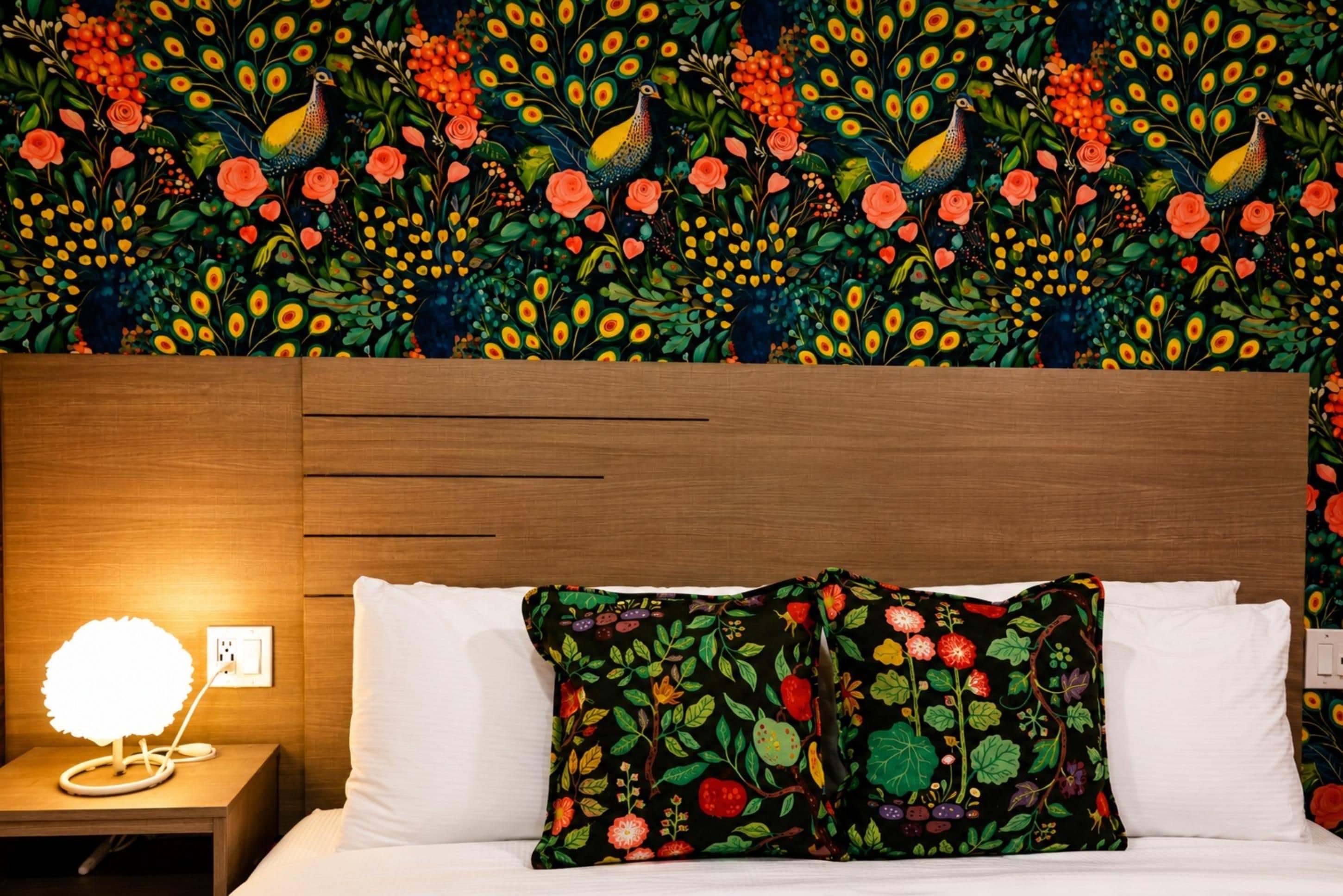 A hotel room with a wooden headboard, white bedding, and a colorful floral-patterned pillow.