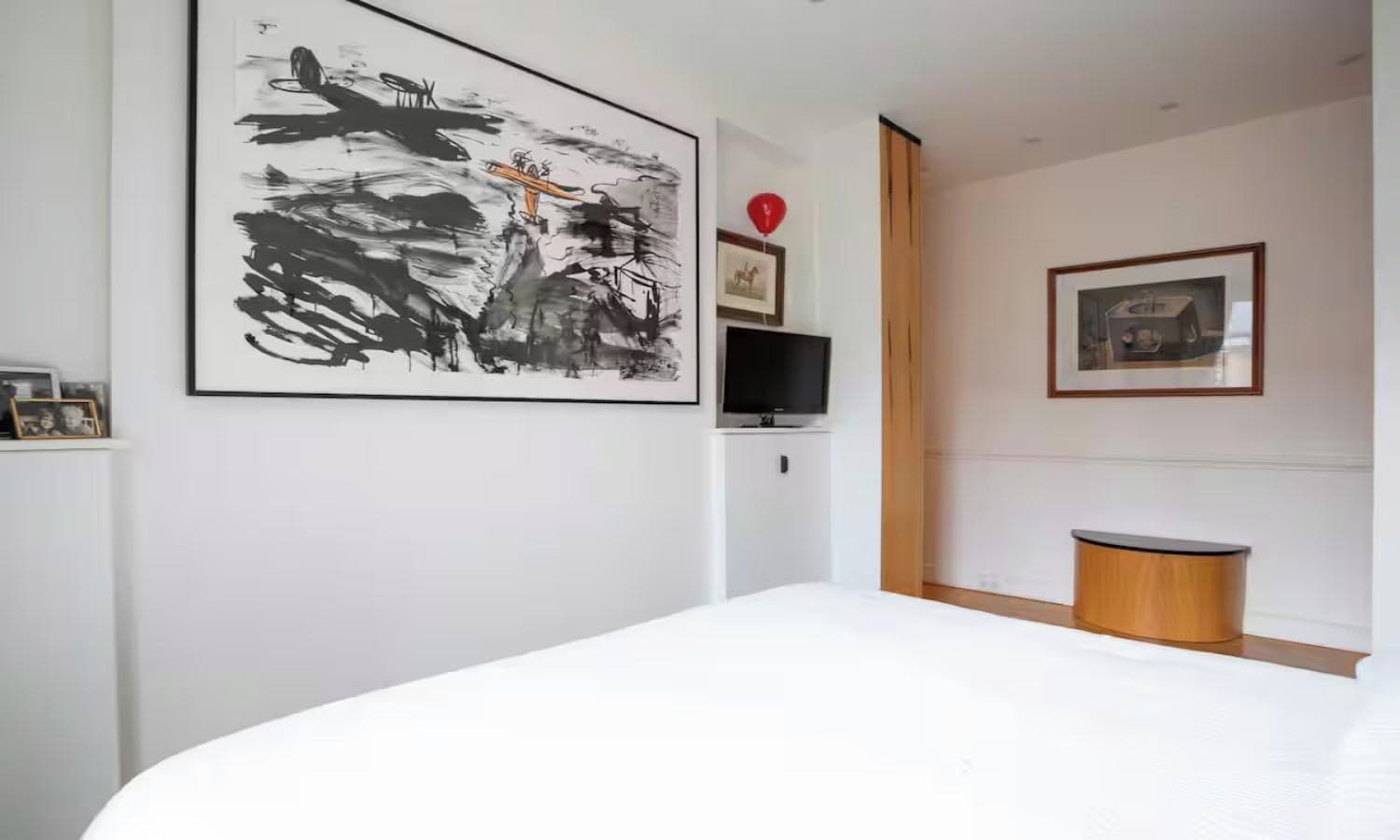 Quarto com uma grande pintura abstrata, uma televisão e uma pequena mesa de madeira.