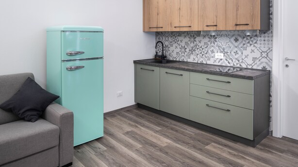 A compact kitchen with a teal refrigerator, wooden cabinets, and a patterned backsplash. - Vrbo Property (Montichiari)