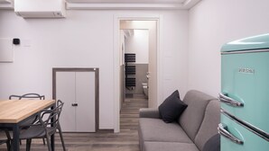A modern kitchen with a teal refrigerator, a dining area with a wooden table and chairs, and a grey sofa with a pillow. - Vrbo Property (Montichiari)