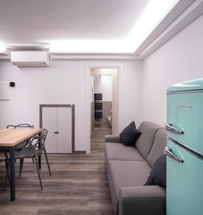 A modern kitchen with a teal refrigerator, a dining area with a wooden table and chairs, and a grey sofa with a pillow. - Vrbo Property (Montichiari)