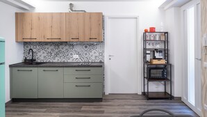 A compact kitchen with green cabinets, a microwave, and a small shelf with kitchen items. - Vrbo Property (Montichiari)