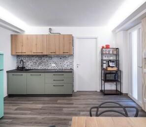 A compact kitchen with green cabinets, a microwave, and a small shelf with kitchen items. - Vrbo Property (Montichiari)