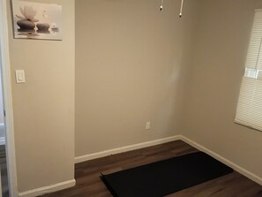 A room with a wooden floor, a black rug, a wall-mounted light fixture, and a window with blinds. - 2-bedroom apartment in charming Atlanta with cool AC and gym access (Atlanta)