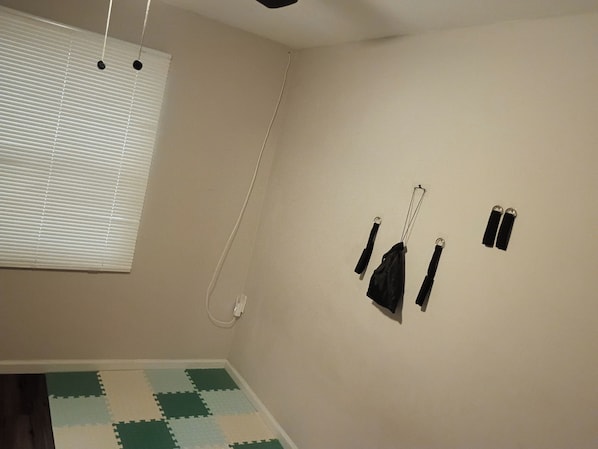 Une pièce dotée d’un ventilateur de plafond, d’une fenêtre avec des stores, d’une prise électrique murale et d’un tapis de sol à carreaux verts et blancs.
