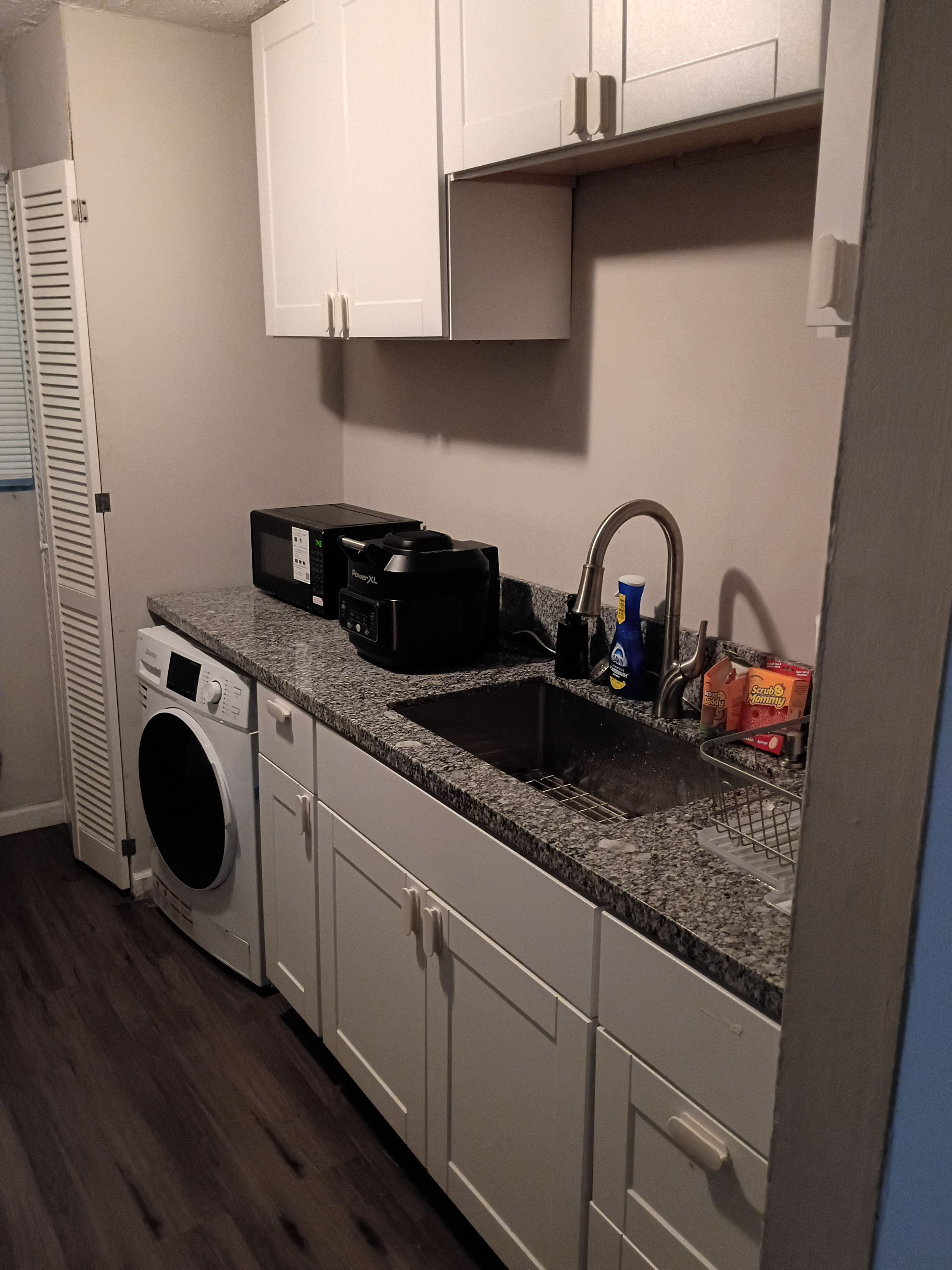 A compact kitchen with a built-in washer, a coffee maker, and a sink with a metal rack.