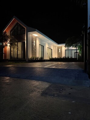 A modern house with a spacious driveway, large windows, and a well-lit exterior.