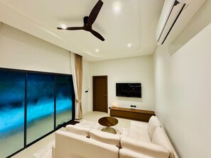 Un salon moderne doté d’un ventilateur de plafond, d’un téléviseur à écran plat, d’un canapé et d’une grande fenêtre offrant une vue dégagée.