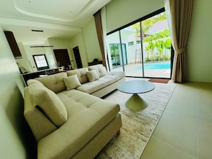 A modern living room with a sectional sofa, a round coffee table, and a view of a swimming pool through large windows.