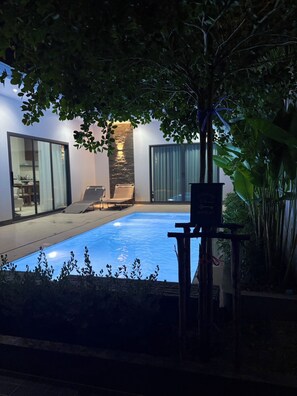 Une piscine à fond de verre, entourée d’un patio aménagé avec des chaises et une table.