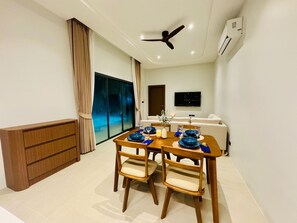 Un espace repas moderne avec une table en bois prévue pour quatre personnes, un ventilateur de plafond et un téléviseur à écran plat fixé au mur.