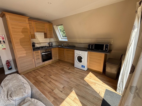 A compact kitchen with wooden cabinets, a built-in oven, a microwave, and a washing machine.