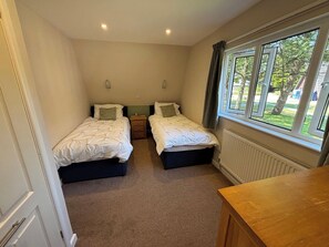 A bedroom with two beds, a nightstand, a window with curtains, and a radiator.