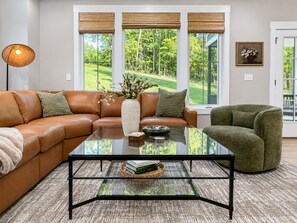 Ein modernes Wohnzimmer mit einem braunen Ledersofa, einem Glastisch und einem grünen Sessel.