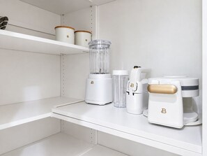 Eine Küche mit weißen Schränken, einem Mixer, einer Kaffeemaschine und einem Glasbehälter auf der Arbeitsfläche.