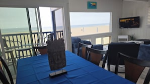 Ein Zimmer mit Tisch für zwei Personen, einem an der Wand befestigten Fernseher und Blick auf den Strand.