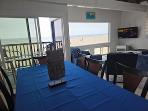 A room with a table set for two, a TV mounted on the wall, and a view of the beach. - BEACHFRONT NEWPORT BEACH-4-bedroom house with panoramic ocean views!! (Newport Beach)