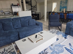 Una sala de estar con un sofá azul, una mesa de centro blanca y un tapete estampado.