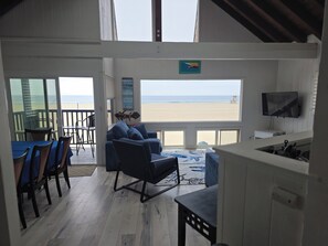 A room with a view of the beach, a TV, and a dining area with chairs and a table. - BEACHFRONT NEWPORT BEACH-4-bedroom house with panoramic ocean views!! (Newport Beach)