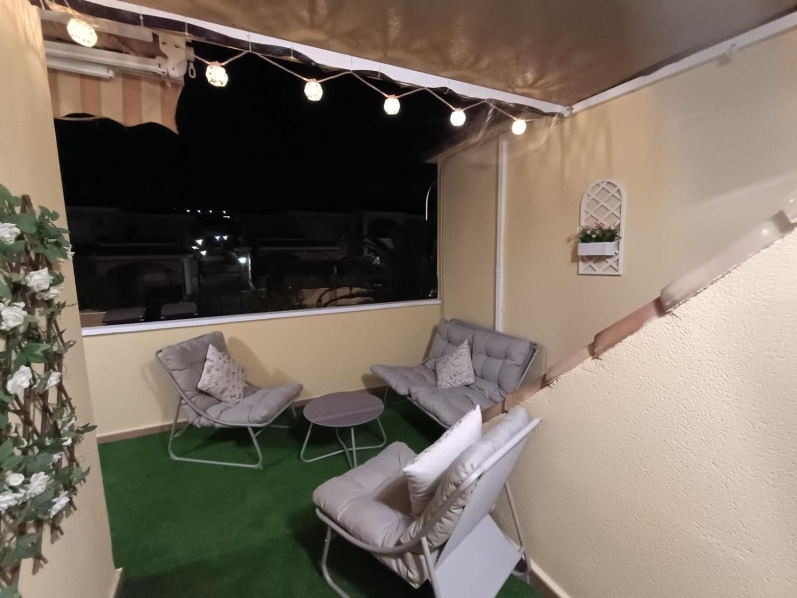 Een balkon met twee grijze fauteuils, een kleine ronde tafel en lichtjes aan een draad.