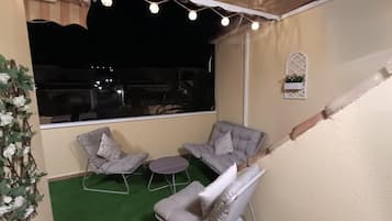 Een balkon met twee grijze fauteuils, een kleine ronde tafel en lichtjes aan een draad.