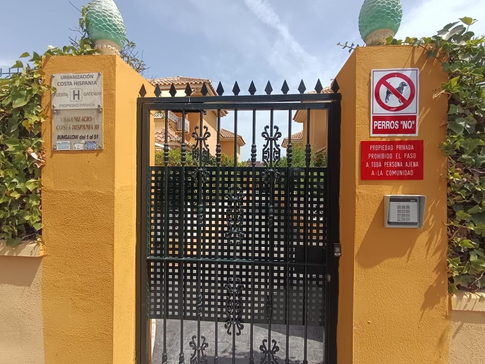 Una entrada cerrada con un portón metálico, un letrero que indica 'No se admiten perros' y un aviso de propiedad privada.