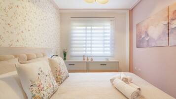 Un dormitorio con cama, cómoda, ventana con persianas y pared con estampado floral.