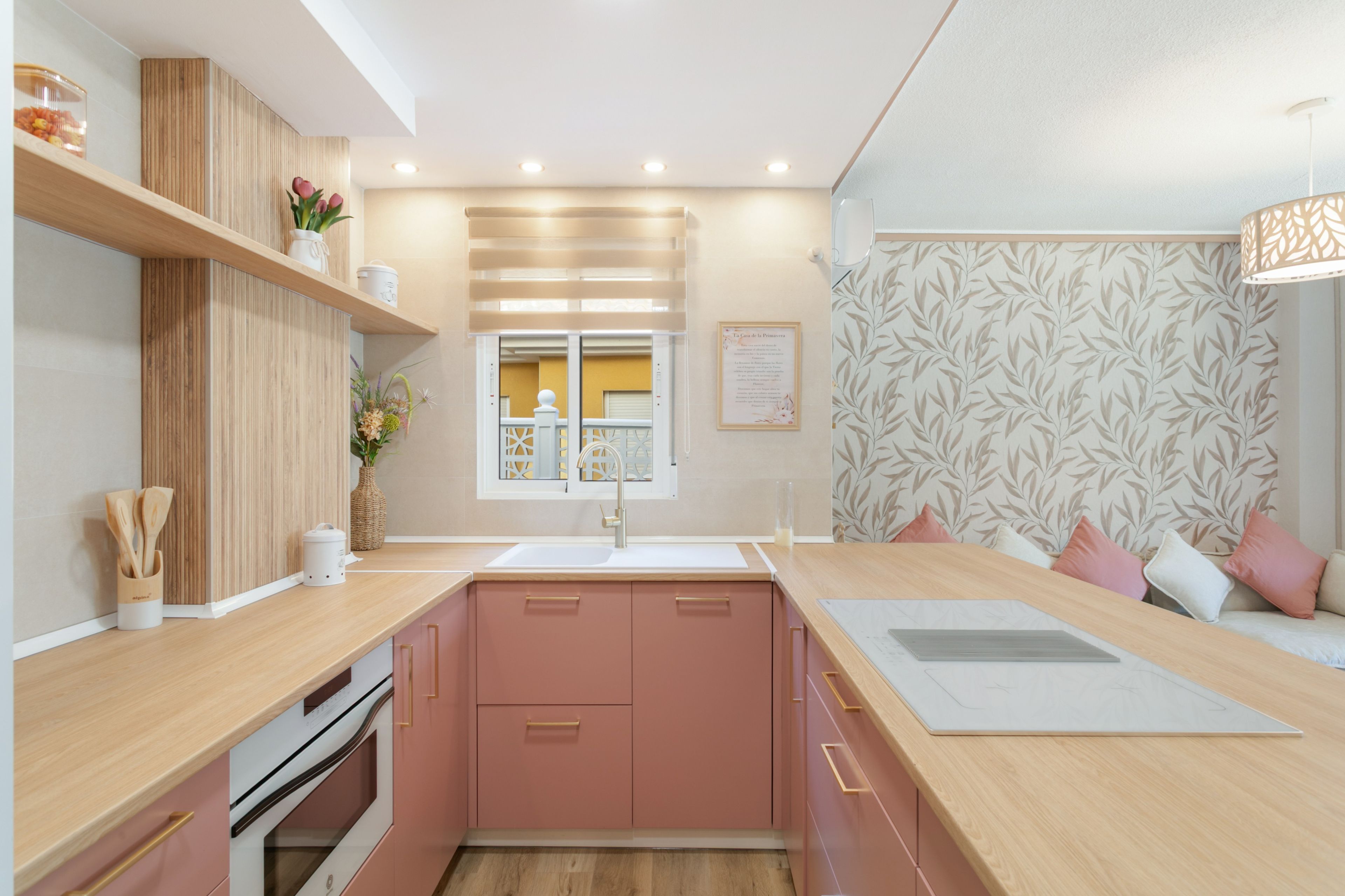 Una cocina moderna con armarios rosa, encimera de madera, horno empotrado y ventana con vistas.