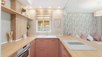 Una cocina moderna con armarios rosa, encimera de madera, horno empotrado y ventana con vistas.
