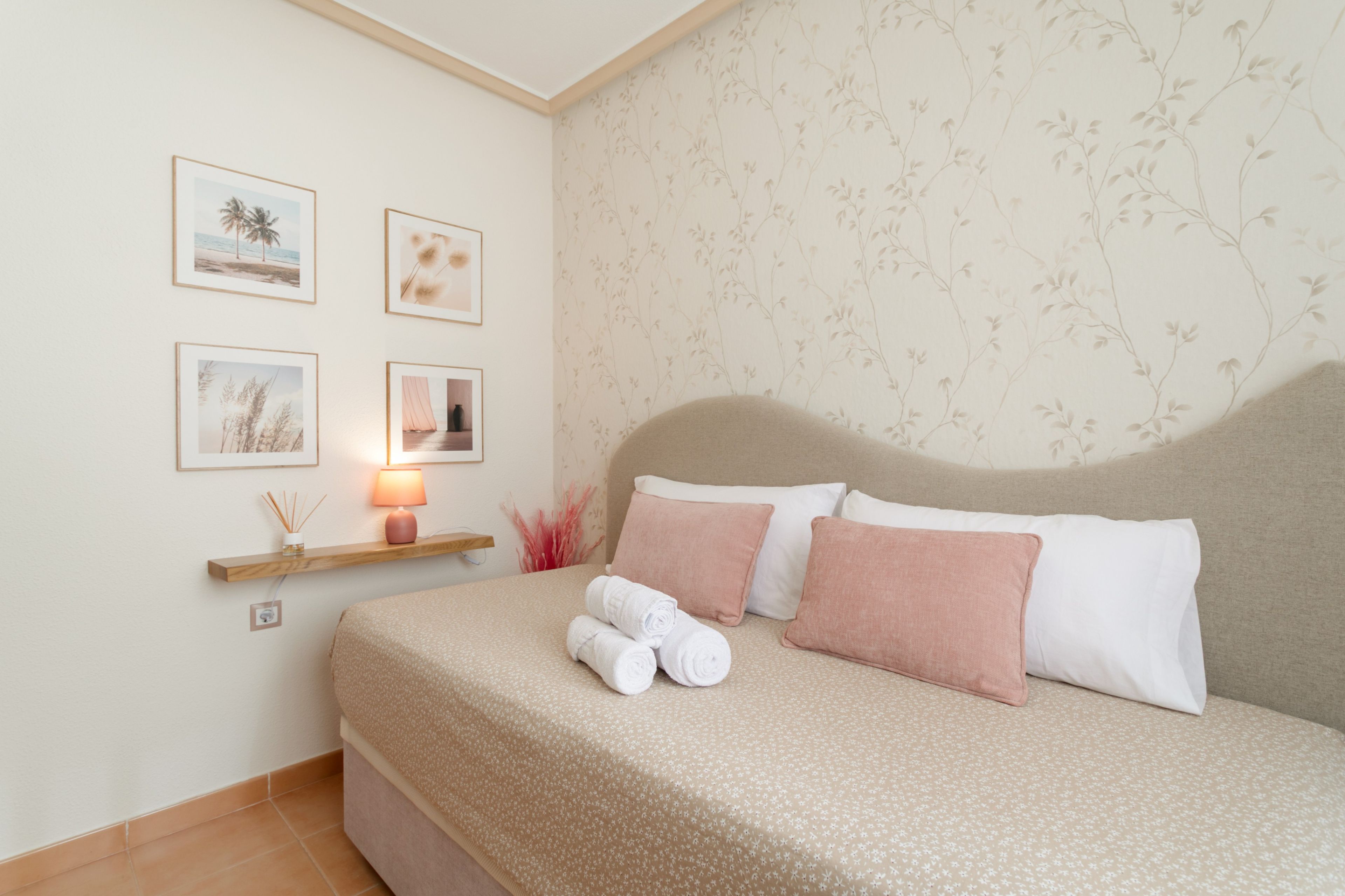 Una cama bien hecha con almohadas y toallas enrolladas, una mesita de noche con una lámpara y cuadros en la pared.