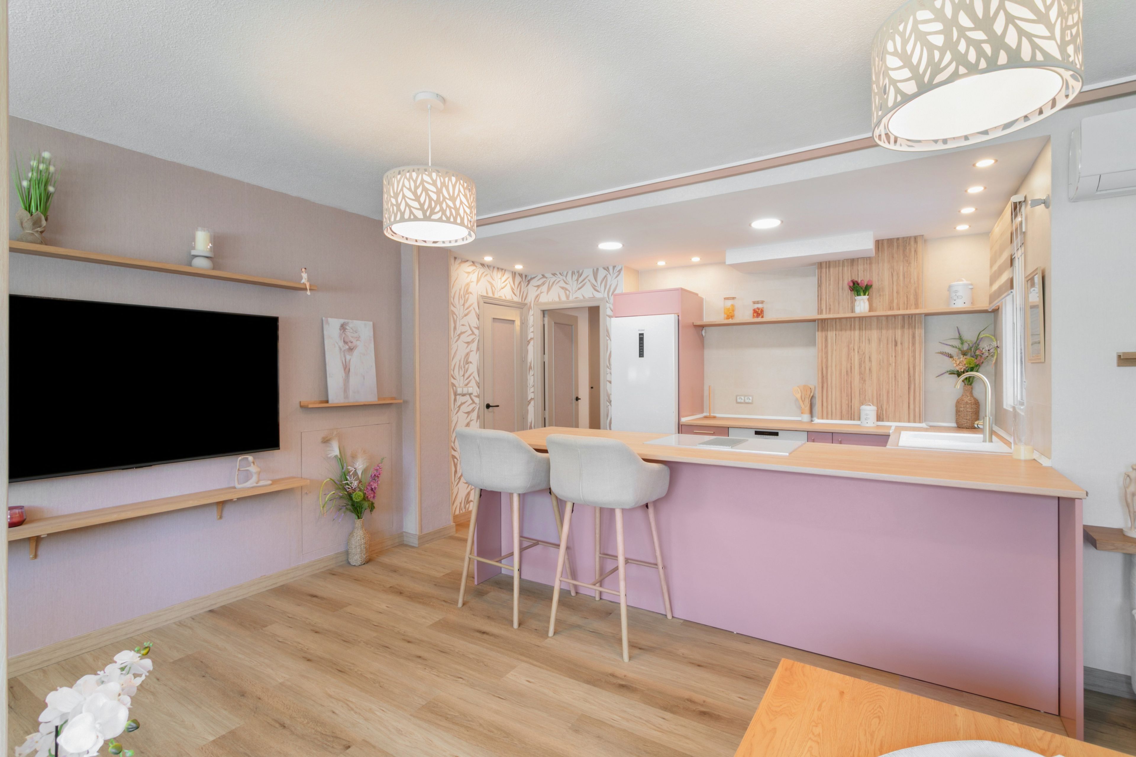 Una cocina moderna con una isla central, taburetes de bar, un televisor de pantalla plana e iluminación colgante.