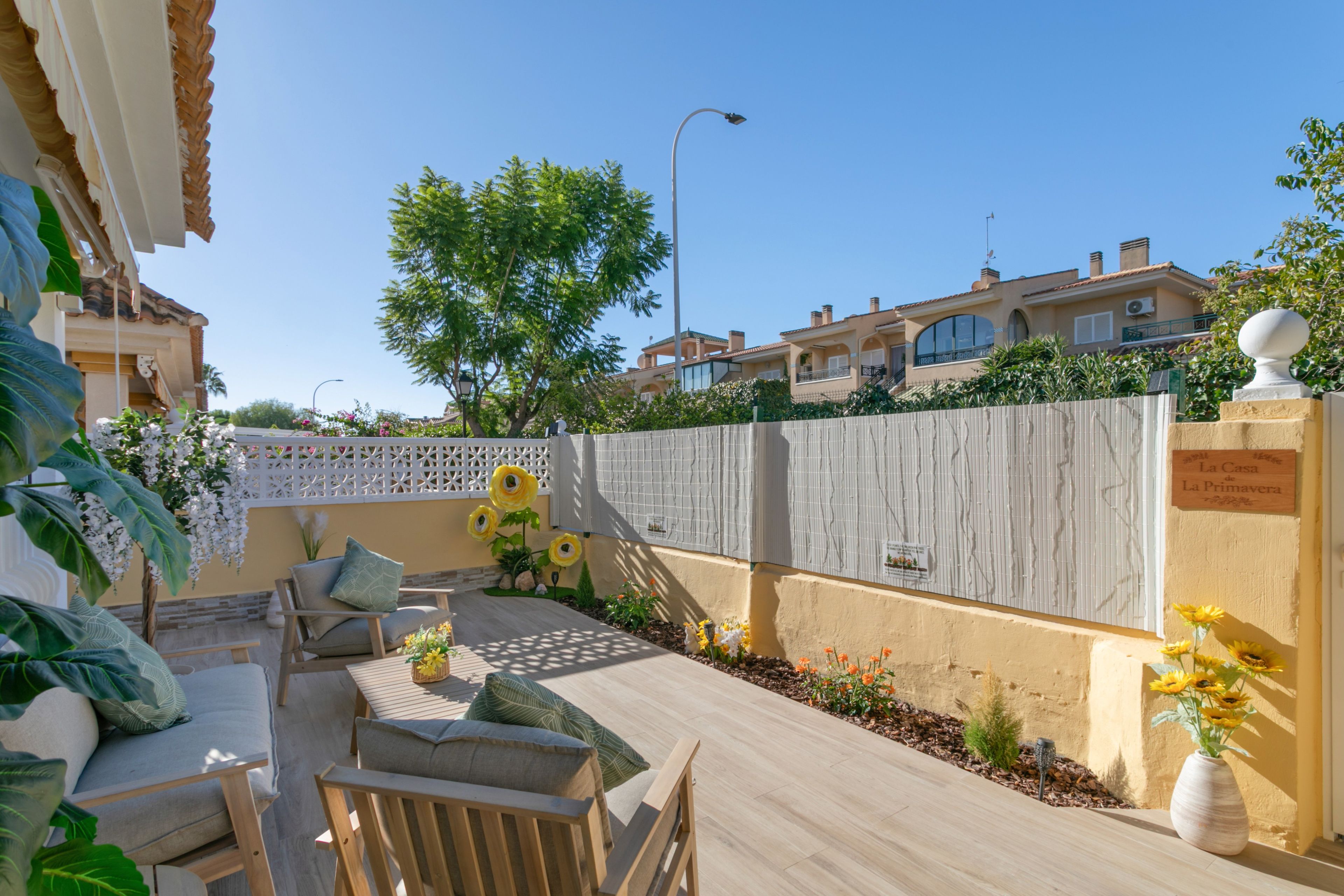 Un patio con mobiliario exterior, un cerco decorativo y un cartel que indica el nombre de la propiedad.
