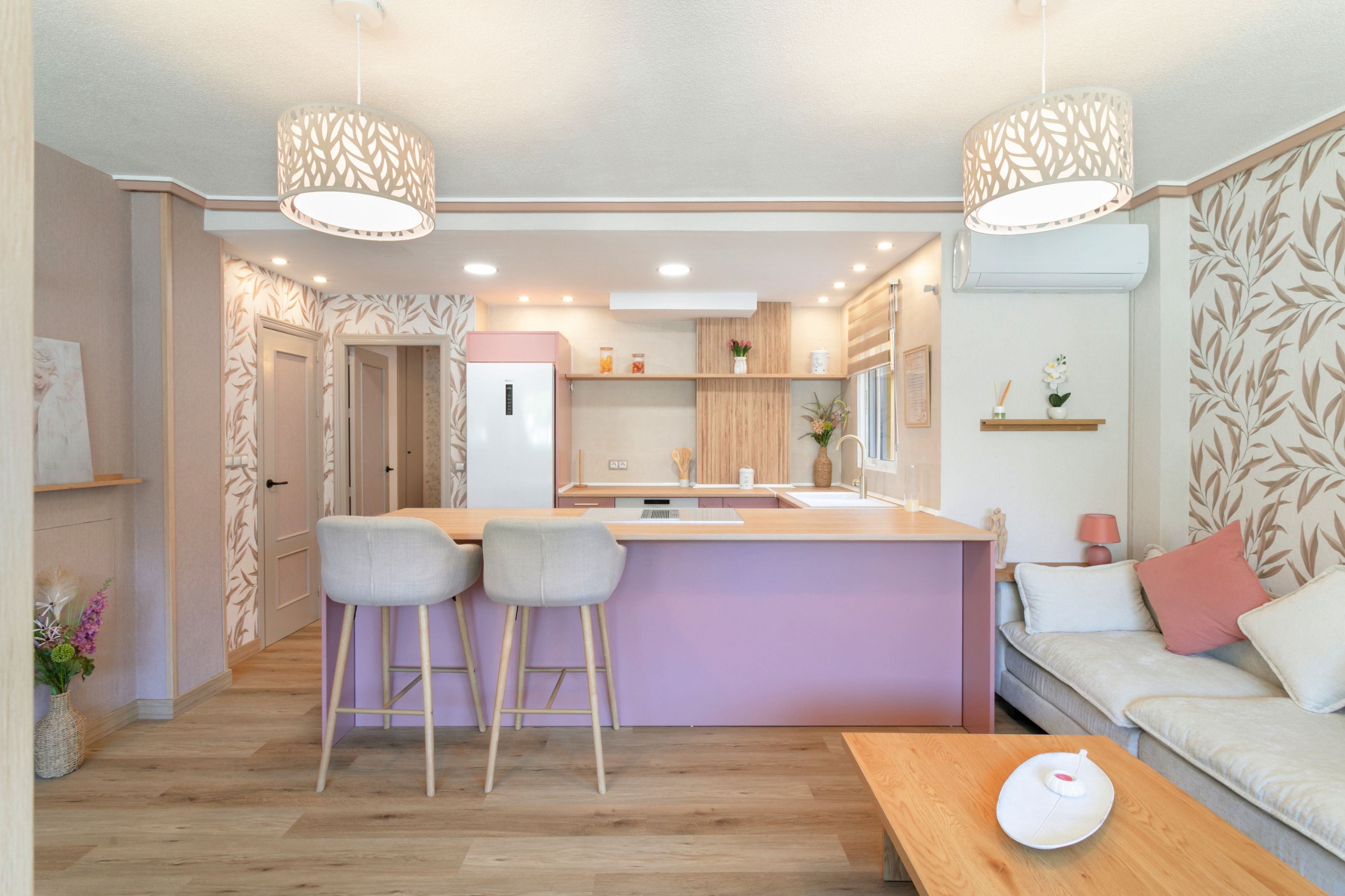A modern kitchen with a central island, bar stools, a dining table, and a sofa with cushions.