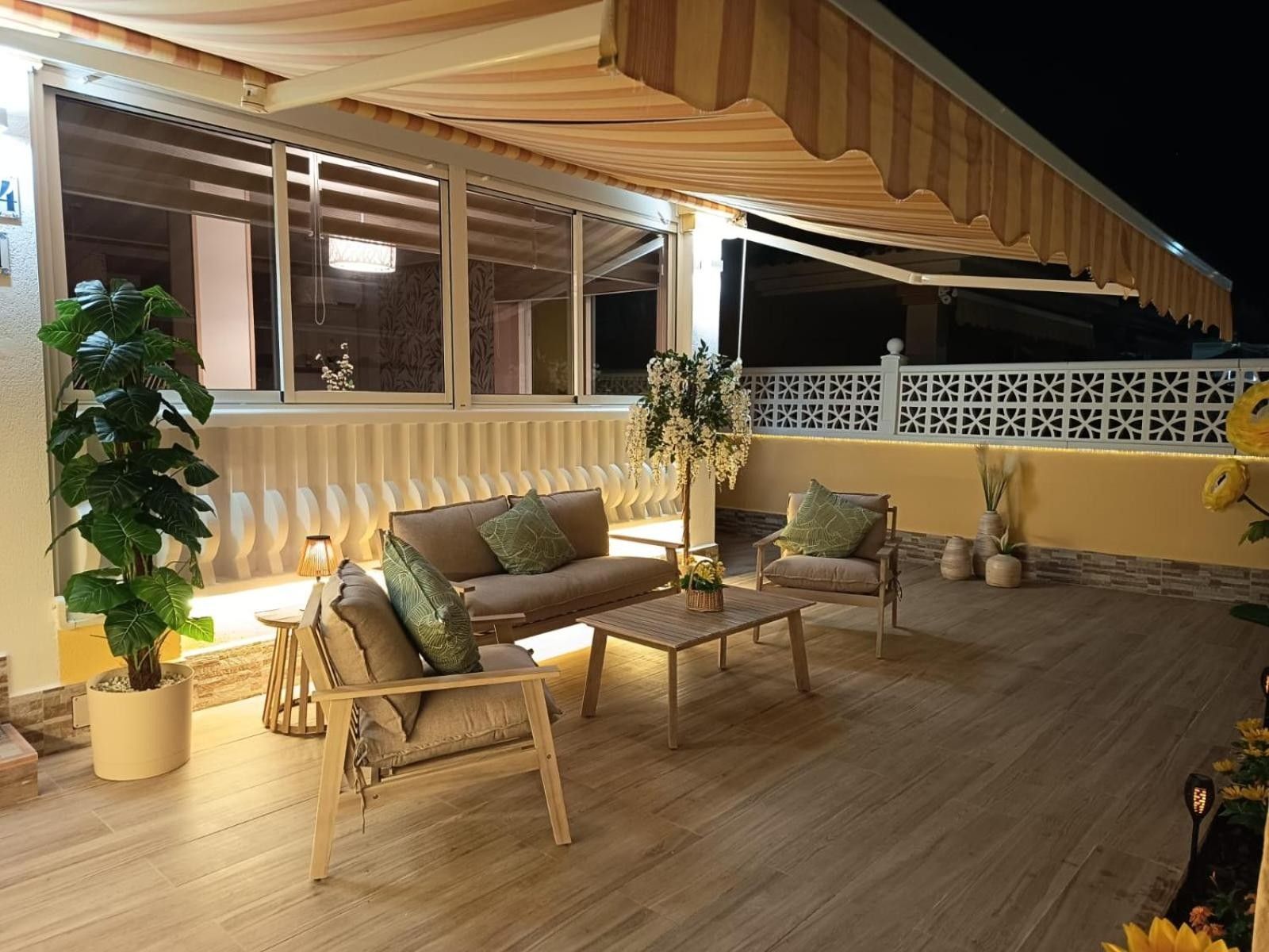 An outdoor seating area with a sofa, chairs, and a table, surrounded by potted plants and a decorative fence.