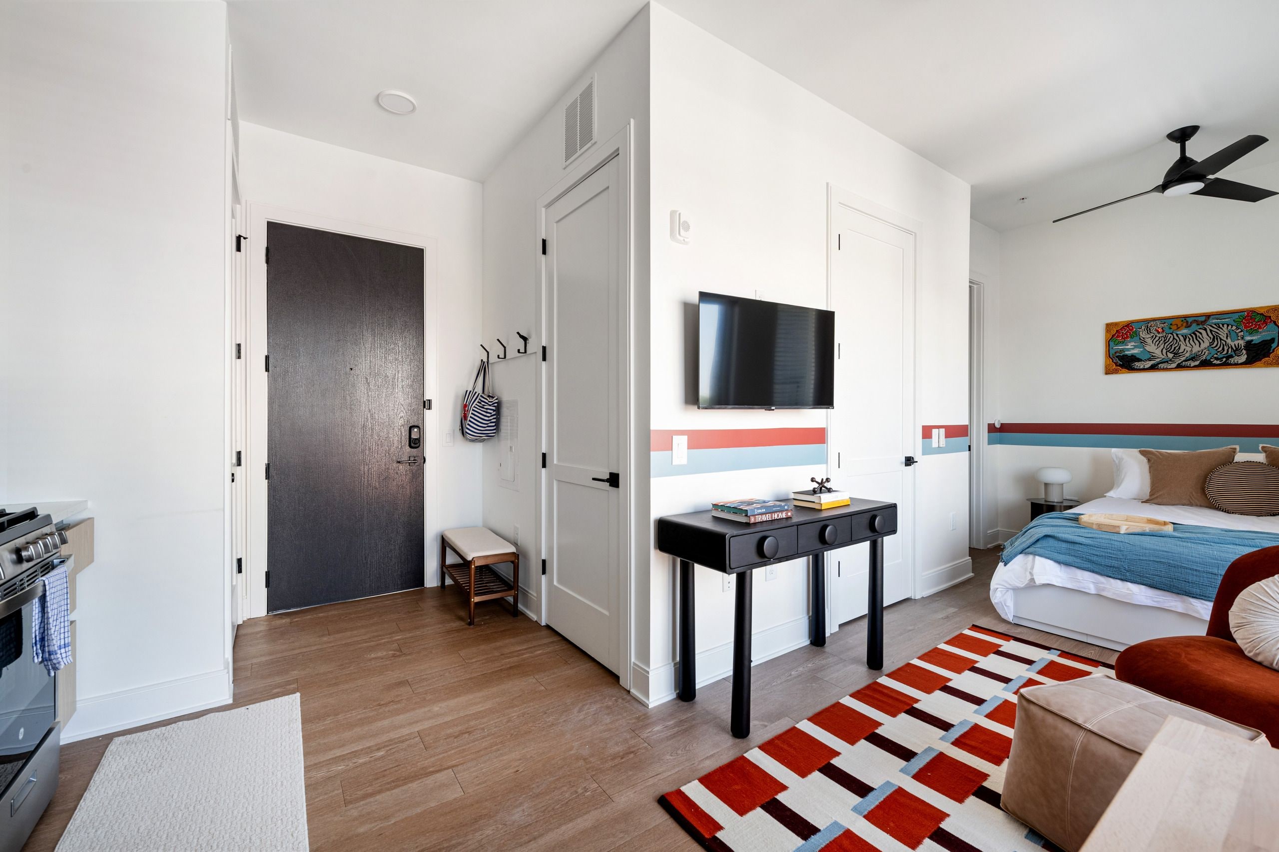 A modern bedroom with a bed, a desk, a TV, and a ceiling fan.