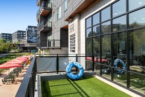 Un edificio moderno con amplios ventanales, mesas al aire libre y una pequeña zona ajardinada con equipo de ejercicio.