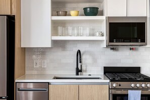 A modern kitchen with white cabinetry, a stainless steel refrigerator, a black faucet, a microwave, and a gas stove. - Ruby Junction (Atlanta)