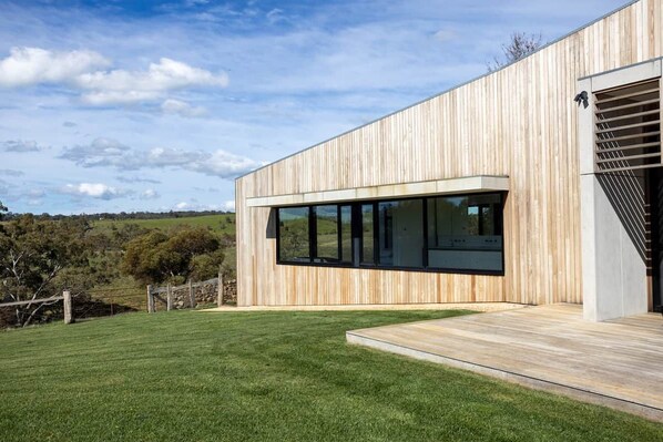 Un bâtiment moderne doté d’une façade en bois, de grandes fenêtres et d’une pelouse verdoyante.
