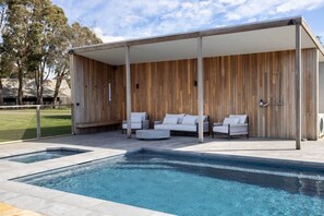 A modern outdoor pool area with a wooden deck, white lounge chairs, and a covered seating area. - FASSWAY FARM - LUXURIATE IN STYLE, TEN MINUTES TO KYNETON (Greenhill)