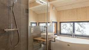 A modern bathroom with a glass-enclosed shower, a freestanding bathtub, and a window providing a view of snow-covered trees. - Cabin in Turrach With Balcony and Wi-fi (Stadl-Predlitz)