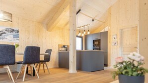 A modern interior with wooden walls and a central island with a kitchen. There are chairs around a table and a potted plant on a table. - Cabin in Turrach With Balcony and Wi-fi (Stadl-Predlitz)