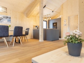 Et moderne interiør med trævægge og en central ø med et køkken. Der er stole omkring et bord og en potteplante på et bord.