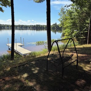 A lake with a dock and a swing chair by the shore. - Mohawksin Magic! Lakeside 2 Bdrm Lower-Level Home & Garage - 3 Miles to Tomahawk (Tomahawk)
