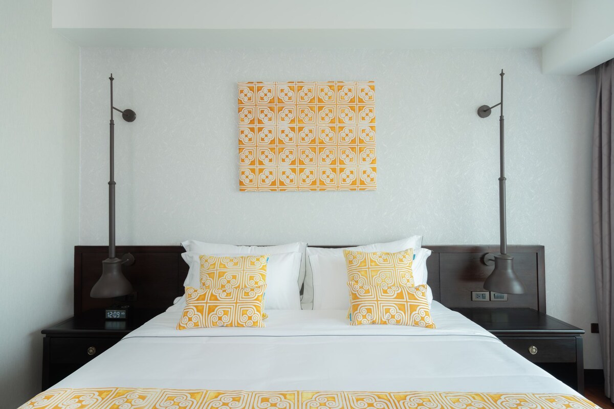 Habitación de hotel con cama, dos mesitas de noche, una obra de arte en la pared y un reloj.
